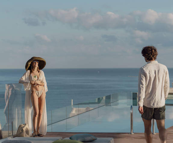Α Woman Stand by the Pool Enjoying the Sun and her Drink as a Man Approaches