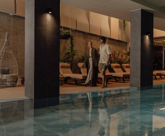 A Couple Walking in The Relaxation Area of the Spa by the Interior Pool
