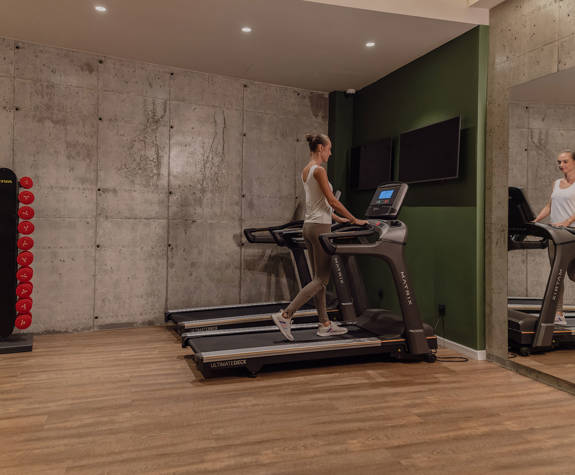 A Woman Running on a Modern Treadmill Next to the Wall Mirrors in the Gym