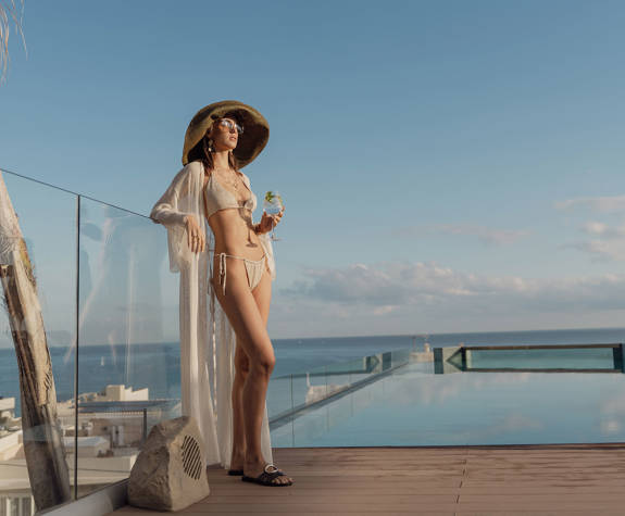 Α Woman Standing by the Pool Enjoying the Sun and her Drink