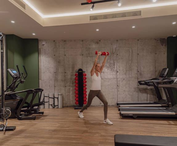 A Woman Working Out with Weights in the Center of the Gym Next to the Training Equipment